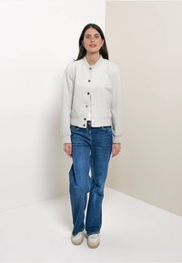 Lichtgrijs sweatshirt met een ronde hals en een knoopsluiting aan de voorkant, gecombineerd met donkerblauwe flared jeans en beige sneakers. Glad, casual stof.