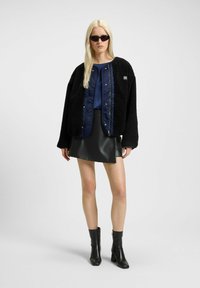 Black fleece bomber jacket over a navy satin top and a black faux leather mini skirt; paired with black ankle boots and sunglasses.