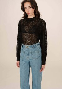 Zwarte kanten top met lange mouwen, ronde hals en doorschijnend ontwerp, gecombineerd met lichtblauwe denim jeans met hoge taille en achterzakken.