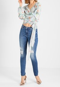 Vaaleansininen kukallinen kietaisupaita puffihihnoilla, vyötärölle solmittuna, yhdistettynä kuluneisiin sinisiin skinny-farkkuihin ja metallisiin korkokenkiin.