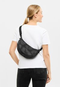 Zwarte slingtas met patroon, kruisbody gedragen, gemaakt van duurzame stof met een verstelbare riem. Beschikt over een gladde textuur en subtiele branding.