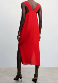 Robe sans manches rouge avec un dos en V, longueur genou et fente sur le côté, réalisée en tissu léger. Présente des bretelles larges et une silhouette fluide.