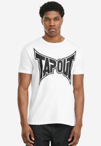 Weißes Baumwoll-T-Shirt mit einem großen schwarzen "TAPOUT"-Logo auf der Vorderseite. Kurze Ärmel und Rundhalsausschnitt.