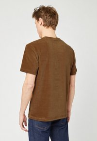 Bruine ribstof t-shirt met een relaxte fit, korte mouwen en een ronde hals. Gelaagde oppervlakte met subtiel ribbelpatroon.