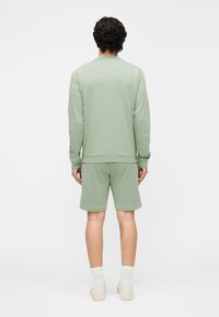 Lichtgroene sweatshirt met lange mouwen en boorden, gecombineerd met bijpassende korte broek. Stof lijkt zacht en gestructureerd. Eenvoudig, casual ontwerp.