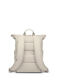 Beige padded backpack with wide shoulder straps, top carry handle, side pockets, and subtle horizontal stitching on back panel.