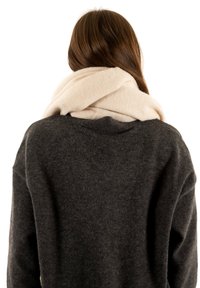 Écharpe en laine beige drapée autour du cou, superposée à un pull gris foncé, texture douce visible. Design minimaliste sans motifs ni accessoires.