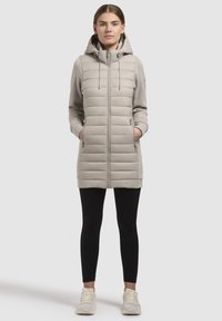 Lys grå puffjakke med hætte, med lynlås foran, sidelommer og ribbede ærmer, parret med sorte leggings og sneakers.