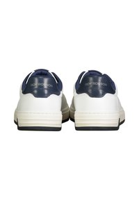 Witte leren sneakers met marineblauwe hielaccenten, voorzien van een rubberen zool, een gewatteerde kraag en een diepterelief logo op de achterkant. Vlak vetersysteem.