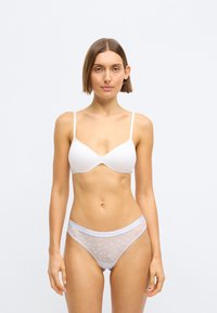 Λευκό σουτιέν με λείες, καλυμμένες θήκες και λεπτές τιράντες; αντιστοιχία λευκά εσώρουχα με διάφανη ύφανση και μοτίβο αστέρια. Βασικός σχεδιασμός, χωρίς επιπλέον στολίδια.