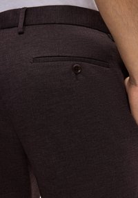 Dunkelbraune Stoffhose mit strukturierter Webart, ausgestattet mit einer Gesäßtasche und einem braunen Knopf sowie einem geraden Beinanschnitt.