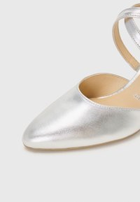 Metallic silver pointed-toe heel with a curved strap across the ankle. Smooth texture with a beige insole and minimalistic design.