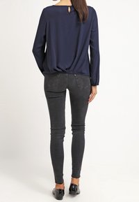 Námořnická modrá halenka s dlouhými rukávy aď slotem na zádech, spárovaná s černými skinny džíny a černými balerínami. Hladká tkanina a přiléhavý silueta.