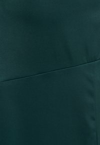 Dunkelgrüner Stoff mit einer glatten, matten Textur. Verfügt über ein sauberes, minimalistisches Design und subtile Nahtdetails.