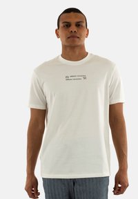 T-shirt blanc à manches courtes avec un col rond, comportant un graphique noir imprimé pour "Armani Exchange" centré sur la poitrine.