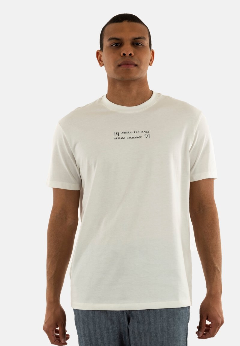 T-shirt blanc à manches courtes avec un col rond, comportant un graphique noir imprimé pour "Armani Exchange" centré sur la poitrine.