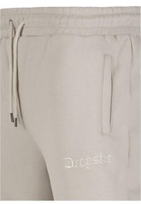 Light gray cotton joggers with an elastic waistband, side pockets, and embroidered "Dropsize" logo in white. Textured fabric finish.
