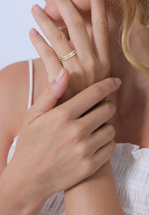 Goldene, grüne und orange gestapelte Ringe an den Fingern. Glatte Oberfläche, dünnes Design, getragen an dem Mittelfinger und Ringfinger einer Hand.