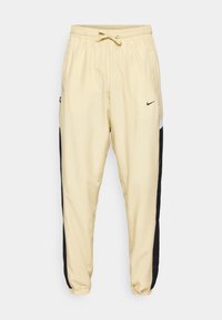 Helle beige Nike Jogginghose mit schwarzen Seitenpanelen, elastischem Bund mit Kordelzug, Seitentaschen und elastischen Bündchen.