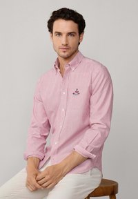 Camisa de hombre de algodón, con rayas verticales rojas y blancas, cuello abotonado y logo bordado en el pecho.