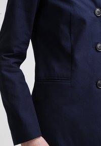 Blazer azul marino con un corte ajustado, tejido texturizado, pecho simple con seis botones y un bolsillo lateral. Acabado suave y forma estructurada.