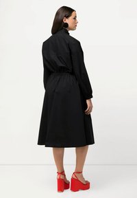 Musta mekko pitkillä hihoilla, vyötäröltä kiristetty ja liehuva hameosa. Yhdistetty punaisiin paksupohjaisiin sandaaleihin, joissa on nilkkahihnat.