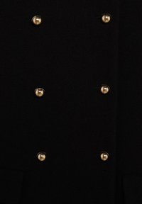 Abrigo negro de lana con diseño cruzado, que cuenta con seis botones metálicos dorados y un tejido texturizado. Detalles incluyen bolsillos con solapa.