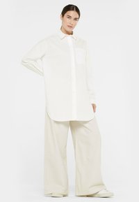 White button-up shirt with long sleeves and a chest pocket, paired with wide beige pants. Soft fabric, relaxed fit, and minimal design.