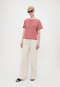 Rød- og hvitstripete t-skjorte kombinert med beige vide bukser. Modellen har på seg svarte solbriller og flate sandaler. Enkel, avslappet design.