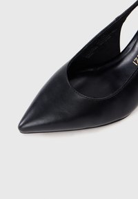 Μαύρο δερμάτινο παπούτσι slingback με μυτερή μύτη, λεία υφή, χαμηλό τακούνι και σχέδιο με κοψίματα στις πλευρές για αερισμό.