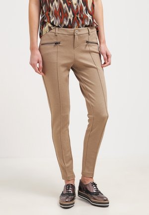 Beige slim-fit broek met voorzakken met rits, gedragen met een mouwloos topje met patroon en metallic platform brogue schoenen.