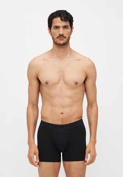 Boxers pretos justos em tecido macio, com uma cintura elástica gravada com o nome da marca, design ajustado e costuras mínimas.