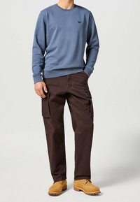 Blå bomullströja med rund hals, bruna cargo-byxor med sidofickor, och tanfärgade stövlar med snörning och gummisulor.