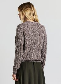 Knit sweater in purple and gray tones with a textured pattern. Ribbed neckline and cuffs, slightly cropped design, paired with a green skirt.