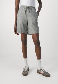 Pantaloni corti grigi con vita elasticizzata e cordino. Presentano tasche e un tessuto testurizzato, abbinati a sneaker con motivo e calzini bianchi fino alla caviglia.
