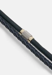 Marineblauwe gevlochten leren armband met een gemarmerde metalen sluiting met een geribbelde patroon. De gladde materiaalcontrasten verhogen de visuele interesse.