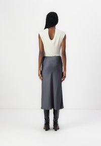 Ermeløs kremtop med nøkkelhull bak, kombinert med et flytende grått satin midi skjørt. Modellen har på seg svarte teksturerte støvler.