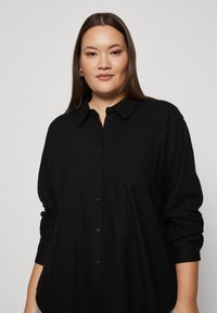Black, long-sleeve button-up shirt with a collar and single chest pocket. Soft fabric, relaxed fit, and subtle texture details.