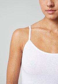 Witte katoenen tanktop met dunne bandjes, met een getailleerd ontwerp en een gladde textuur, die de schouder- en halslijn benadrukt.