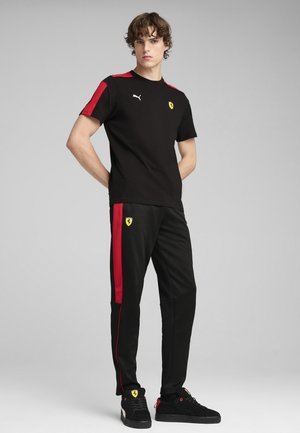 Black T-shirt with red accents, featuring Puma logo and Ferrari emblem. Black track pants with red side stripes, paired with black sneakers.