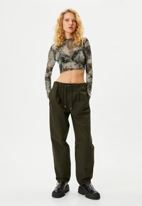 Crop top med ett genomskinligt, batikmönster i grått och grönt, parat med löst sittande mörkgröna byxor och svarta tjocka kängor.