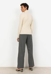 Cream ribbed turtleneck sweater with fitted design, paired with grey pinstripe wide-leg trousers and black patterned heeled sandals.