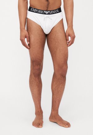 Weiße Schwimmshorts mit Kordelzug, ausgestattet mit einem schwarzen, markierten Bund. Glatte Textur, enganliegendes Design und minimaler Schnitt.