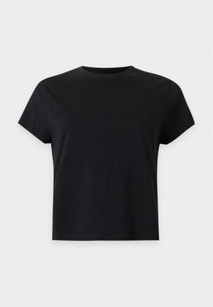 Kobieta w czarnym t-shircie, szerokich spranych szarych dżinsach z czarnym paskiem i czarnych spiczastych butach z srebrnymi ćwiekami.