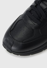 Black athletic shoe with a textured leather upper, perforations for breathability, flat laces, and a sturdy rubber sole.