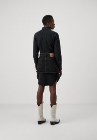 Zwarte denimjas met een kraag en lange mouwen; gecombineerd met een bijpassende denimrok met een rafelige zoom. Witte cowboylaarzen als schoeisel.