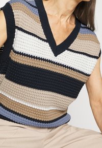 Stickad ärmlös topp med V-ringning, horisontella ränder i marinblått, beige, vitt och ljusblått, med en texturerad, öppen vävdesign.