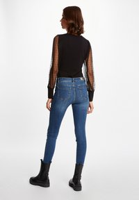 Top nero con maniche a sbuffo trasparenti e a pois, abbinato a jeans aderenti blu e stivaletti neri alla caviglia. Look casual dallo stile contemporaneo.