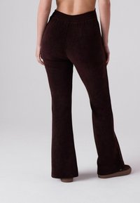 Braune, ausgestellte Hosen aus weichem Stoff mit strukturiertem Finish. Verfügt über einen elastischen Bund und eine glatte, schmale Passform entlang der Beine.