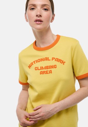 T-shirt en coton jaune avec encolure et poignets de manches côtelés orange. Présente un texte audacieux et incurvé indiquant "ZONE ESCALADE DU PARC NATIONAL".